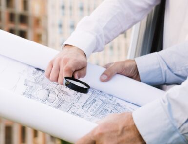 Deux hommes tiennent un plan d'architecture avec une loupe dans la main