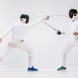 Deux hommes portant une combinaison d'escrime, pratiquant avec une épée sur un fond blanc